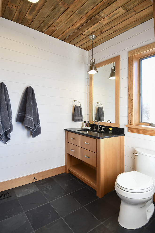 Immagine di una stanza da bagno country con ante lisce, ante in legno scuro, WC a due pezzi, pareti bianche, lavabo sottopiano, pavimento nero e top nero