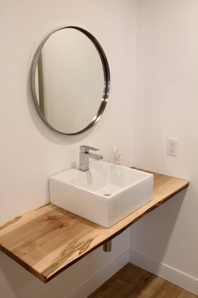 Cette photo montre une salle de bain scandinave de taille moyenne avec un mur blanc, un sol en bois brun, une vasque, un plan de toilette en bois et un sol marron.