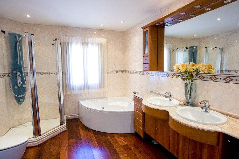 Example of a mid-sized country master beige tile and stone slab medium tone wood floor bathroom design in Sussex with flat-panel cabinets, medium tone wood cabinets, a one-piece toilet, beige walls, a drop-in sink and quartz countertops