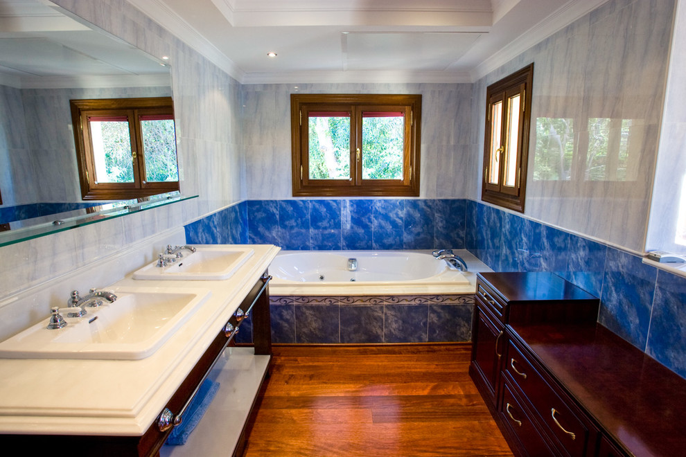 Inspiration för ett mellanstort lantligt en-suite badrum, med släta luckor, skåp i mörkt trä, ett badkar i en alkov, blå kakel, keramikplattor, blå väggar, mellanmörkt trägolv, ett nedsänkt handfat och marmorbänkskiva