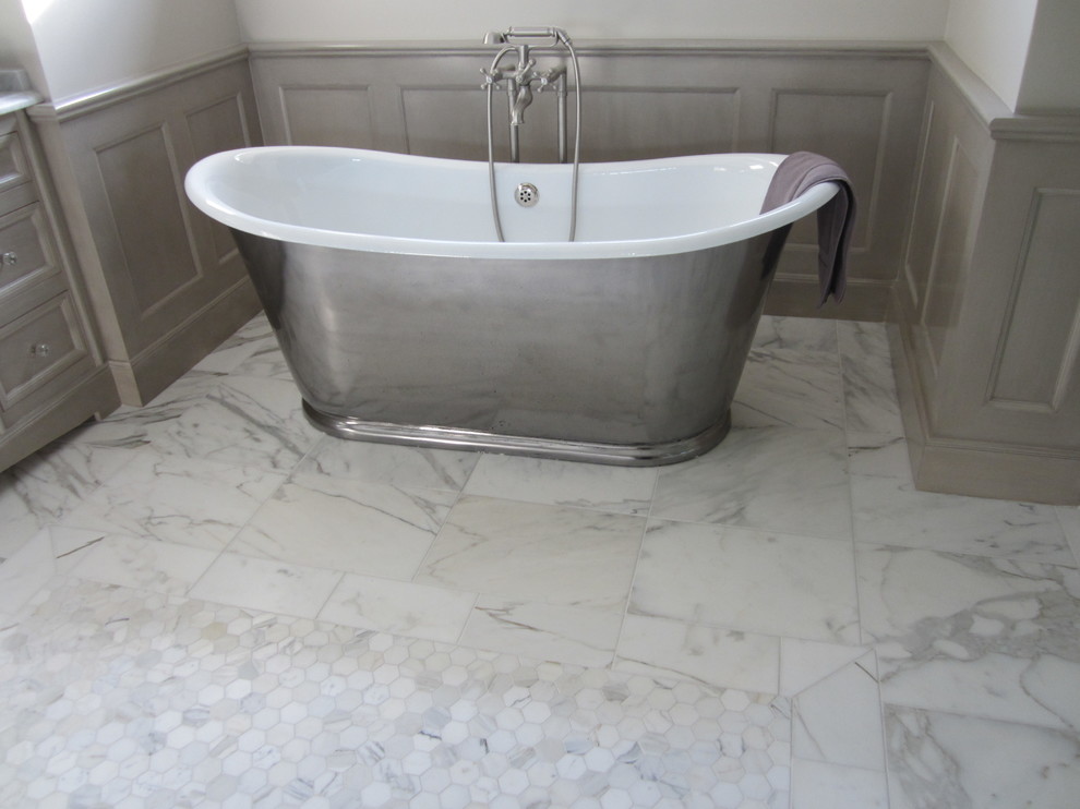 Klassisk inredning av ett badrum, med ett fristående badkar, vita väggar och marmorgolv