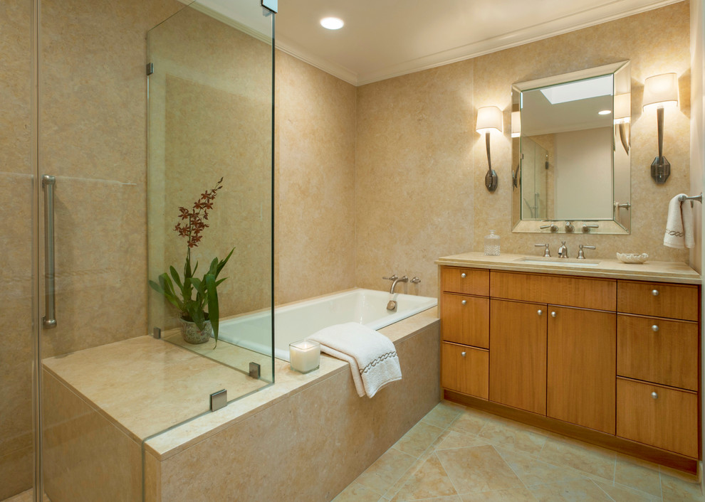 Example of a trendy master stone slab marble floor drop-in bathtub design in New York with an undermount sink, flat-panel cabinets, light wood cabinets and marble countertops