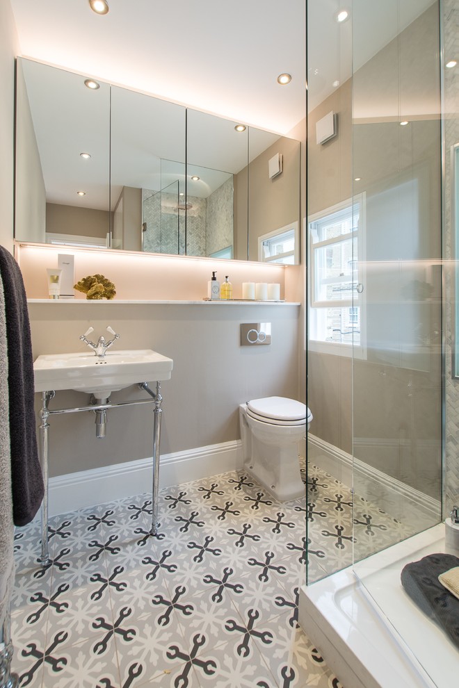 This is an example of a medium sized contemporary ensuite bathroom in London with flat-panel cabinets, a corner shower, a wall mounted toilet, white tiles, marble tiles, beige walls, ceramic flooring, a pedestal sink, marble worktops, multi-coloured floors and a hinged door.