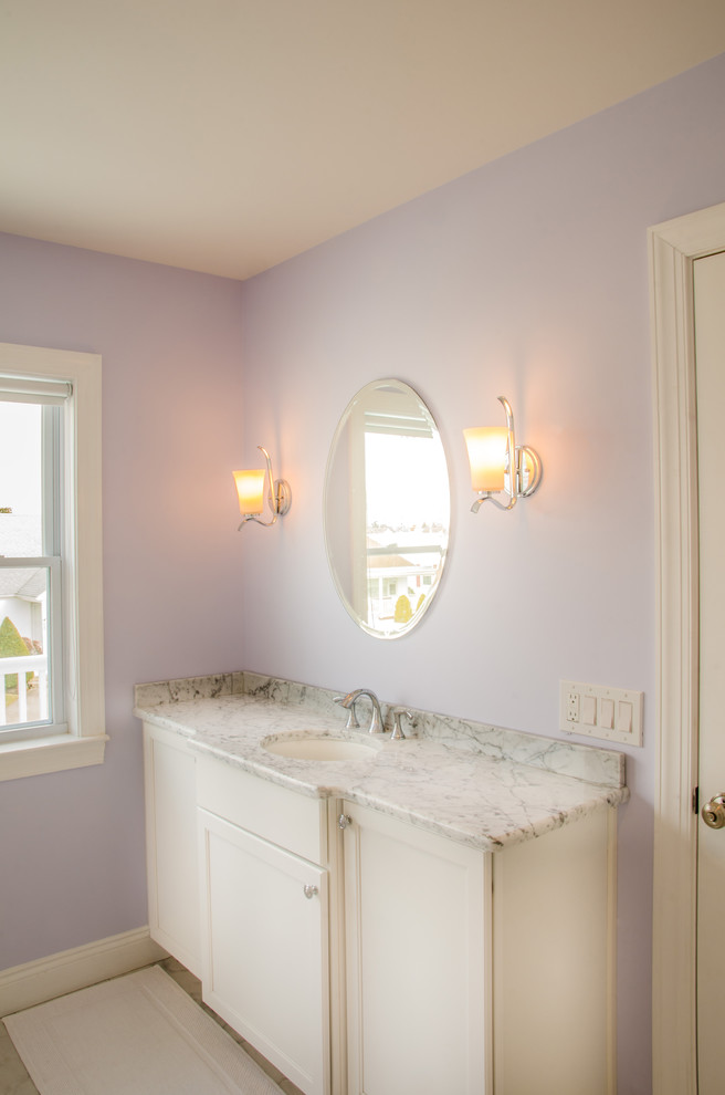 Ispirazione per una stanza da bagno costiera con lavabo sottopiano, ante con riquadro incassato, ante beige, top in marmo e pareti viola