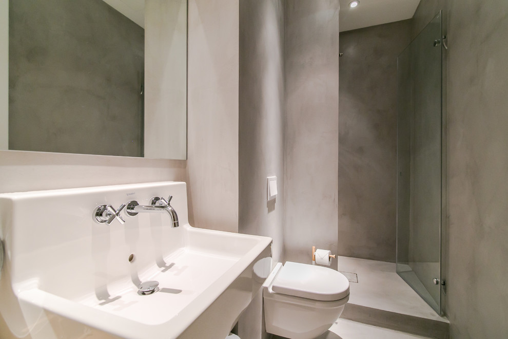 Modelo de cuarto de baño nórdico de tamaño medio con ducha esquinera, sanitario de pared, paredes grises, suelo de cemento, aseo y ducha y lavabo integrado