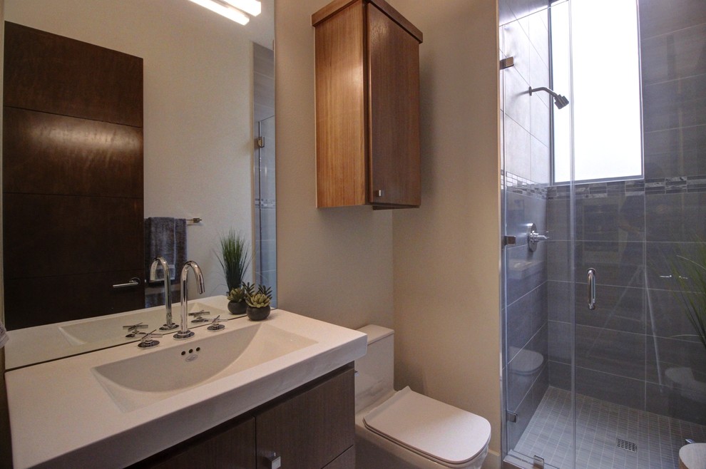 Mid-sized trendy corner shower photo in Austin with flat-panel cabinets, medium tone wood cabinets, a one-piece toilet, beige walls, an integrated sink and quartz countertops