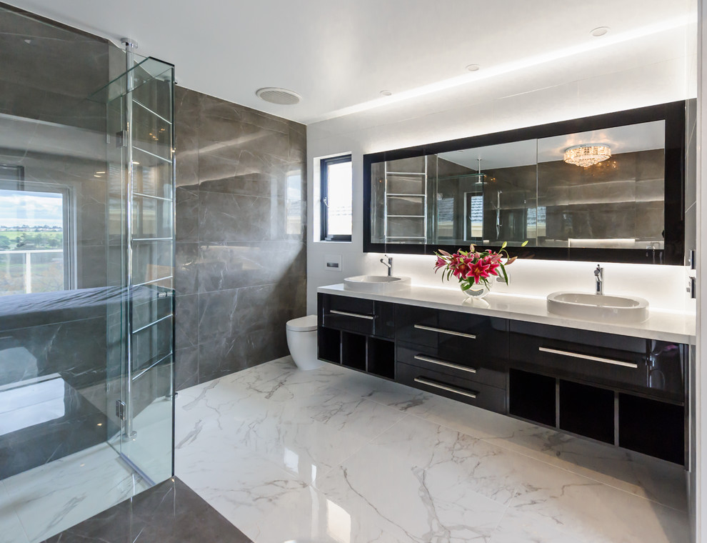 Design ideas for a large modern bathroom in Melbourne with a vessel sink, flat-panel cabinets, black cabinets, engineered stone worktops, a freestanding bath, a walk-in shower, a one-piece toilet, grey tiles, stone tiles, grey walls and porcelain flooring.