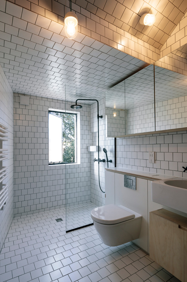 This is an example of a scandinavian family bathroom in London with flat-panel cabinets, white cabinets, a built-in shower, a wall mounted toilet, white tiles, ceramic tiles, white walls, ceramic flooring, a vessel sink, wooden worktops, white floors, an open shower and white worktops.
