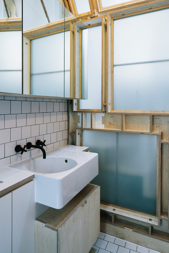Scandi bathroom in London with flat-panel cabinets, light wood cabinets, white tiles, a wall-mounted sink and white floors.