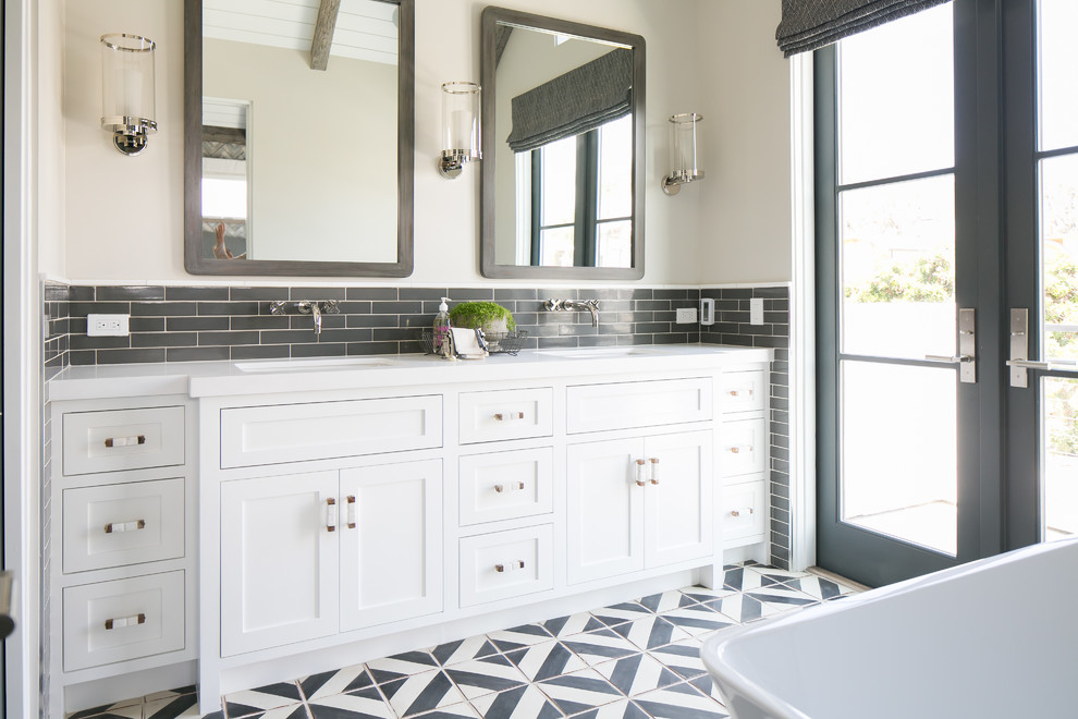 На фото: ванная комната в морском стиле с врезной раковиной, фасадами в стиле шейкер, белыми фасадами, отдельно стоящей ванной, серой плиткой, белыми стенами и разноцветным полом
