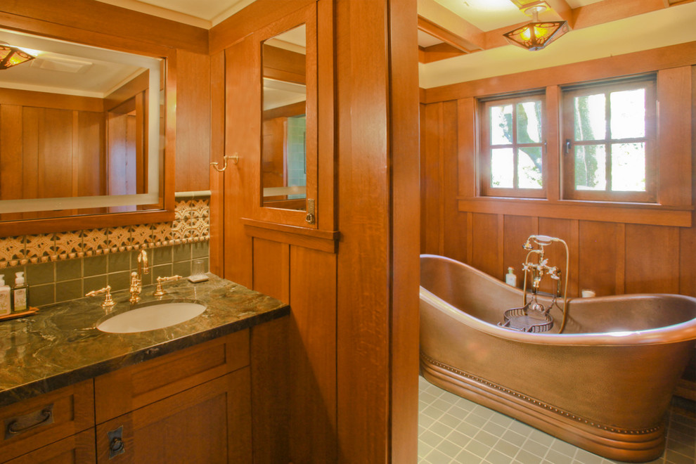 Aménagement d'une douche en alcôve craftsman en bois brun avec un lavabo encastré, un placard avec porte à panneau encastré, un plan de toilette en marbre, une baignoire indépendante, un carrelage vert et des carreaux de céramique.