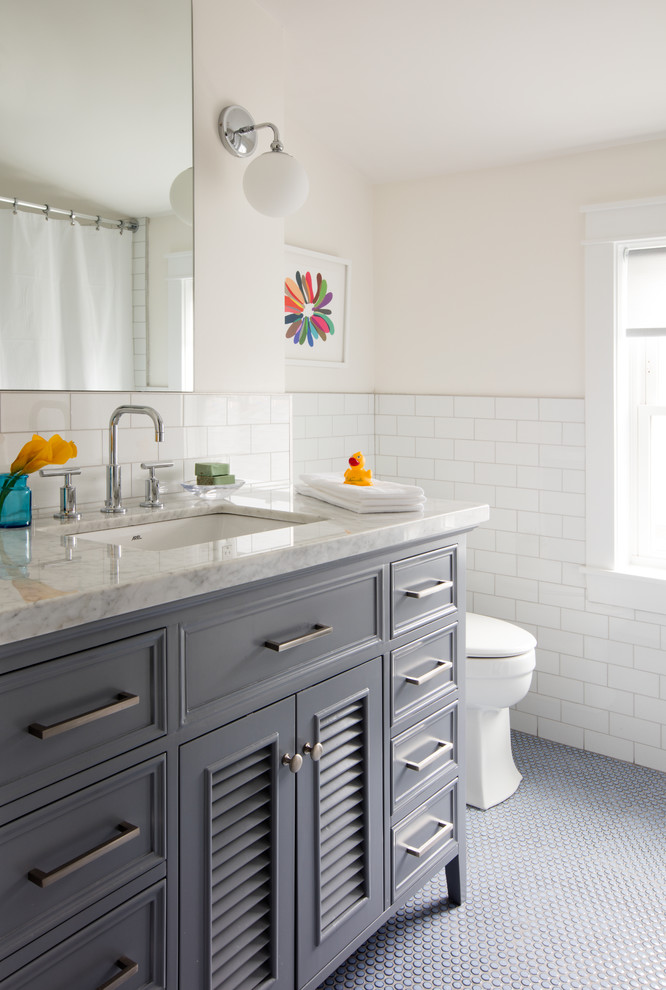 Bild på ett litet vintage grå grått badrum med dusch, med luckor med lamellpanel, grå skåp, en toalettstol med hel cisternkåpa, vit kakel, tunnelbanekakel, vita väggar, ett undermonterad handfat, marmorbänkskiva och grått golv