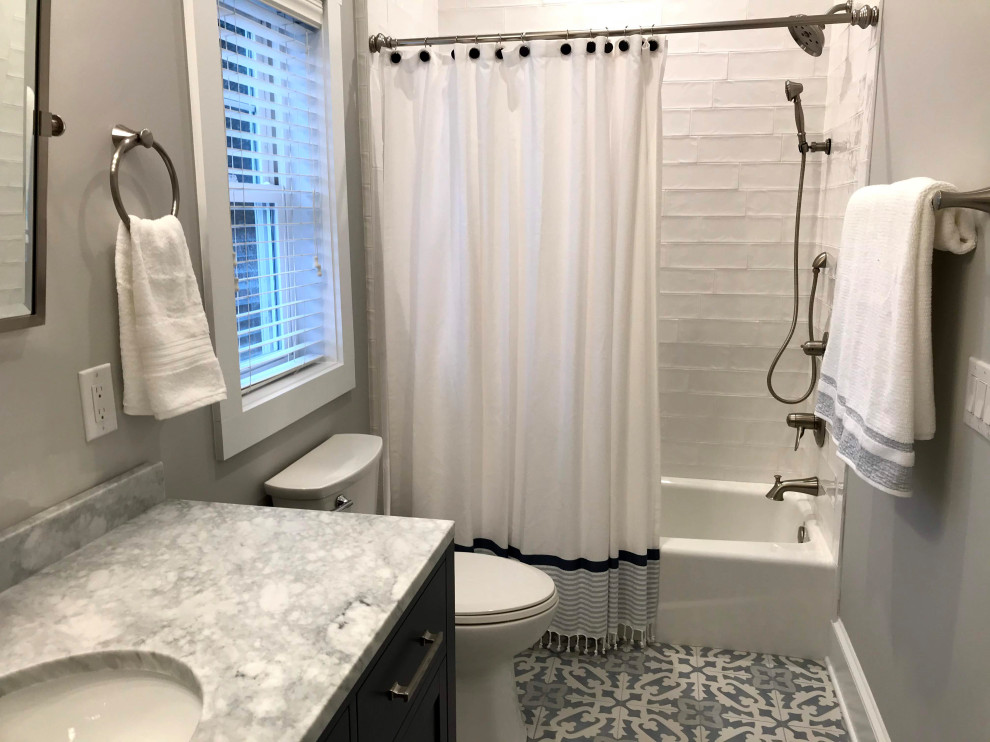 This is an example of an expansive nautical family bathroom in Other with shaker cabinets, a two-piece toilet, white tiles, porcelain tiles, grey walls, a submerged sink, engineered stone worktops, a freestanding vanity unit, porcelain flooring, blue cabinets, a shower/bath combination, blue floors, a shower curtain, grey worktops, an enclosed toilet and a single sink.