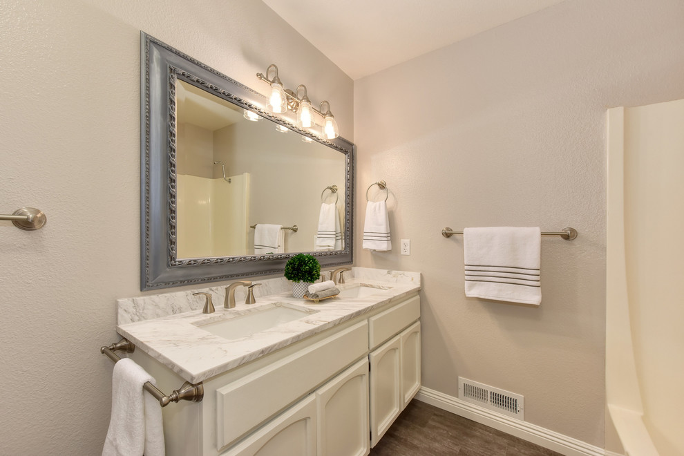 Bild på ett mellanstort vintage vit vitt en-suite badrum, med luckor med infälld panel, vita skåp, ett badkar i en alkov, en dusch/badkar-kombination, grå väggar, mellanmörkt trägolv, ett undermonterad handfat, marmorbänkskiva, brunt golv och dusch med duschdraperi