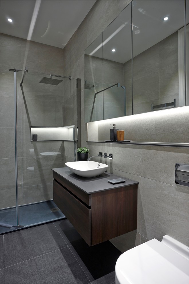 Cette image montre une salle de bain en bois foncé avec un placard à porte plane, une douche ouverte, WC suspendus, un carrelage gris, un carrelage de pierre, un mur gris, un sol en ardoise, une vasque et un plan de toilette en quartz modifié.
