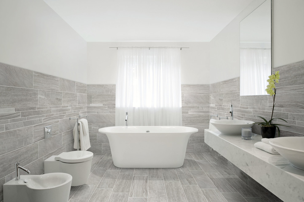 Idéer för funkis badrum, med ett fristående badkar, grå kakel, grå väggar och ett fristående handfat