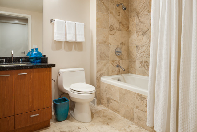 Cette image montre une petite salle d'eau minimaliste en bois brun avec un lavabo encastré, un placard à porte plane, un plan de toilette en marbre, une baignoire posée, un combiné douche/baignoire, WC à poser, un carrelage beige, un carrelage de pierre, un mur beige et un sol en marbre.