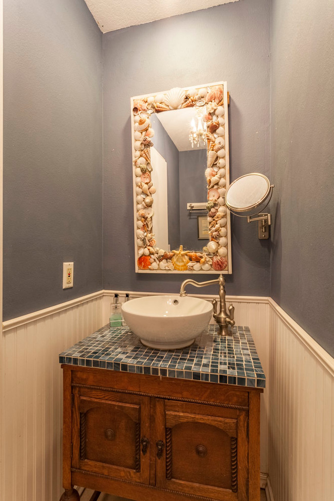 Cette image montre un petit WC et toilettes marin en bois foncé avec un placard en trompe-l'oeil, WC à poser, un carrelage bleu, des plaques de verre, un mur bleu, un sol en carrelage de céramique, une vasque et un plan de toilette en verre.