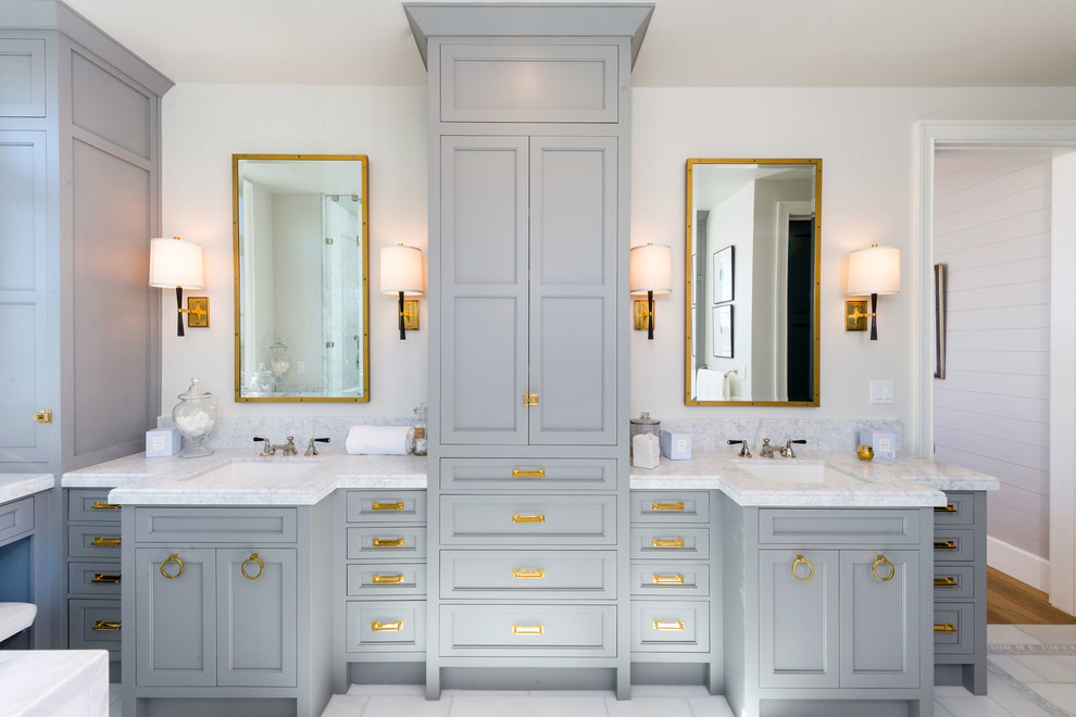 Cette image montre une grande salle de bain principale traditionnelle avec un placard avec porte à panneau encastré, des portes de placard grises, un mur beige, un sol en marbre, un lavabo encastré, un plan de toilette en marbre et un sol gris.