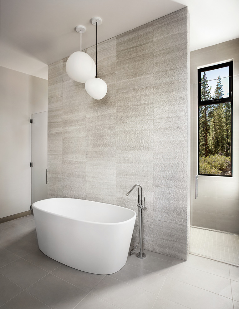 Modelo de cuarto de baño contemporáneo con bañera exenta, baldosas y/o azulejos grises, paredes grises y ventanas