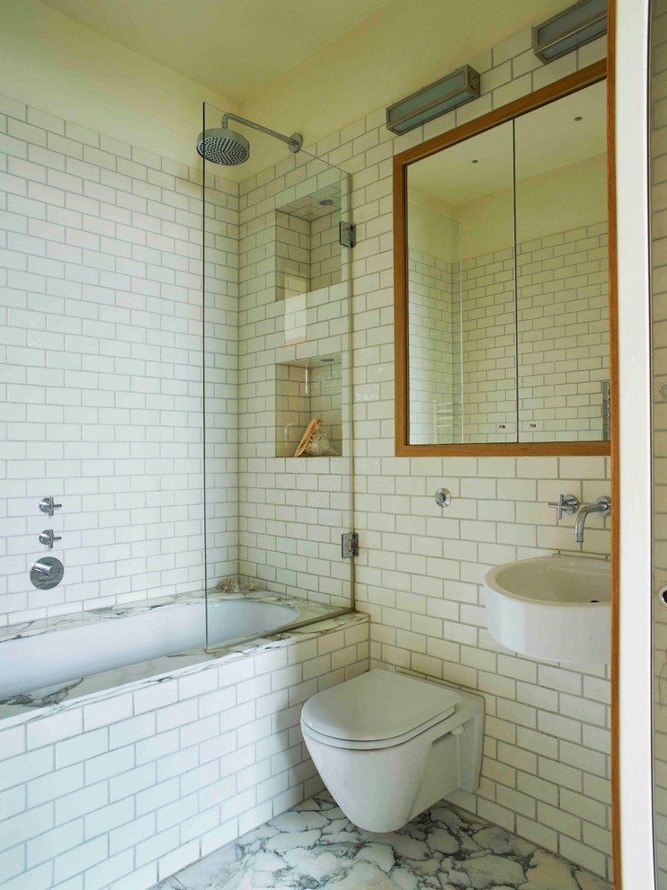 Aménagement d'une petite salle de bain principale éclectique avec des portes de placard blanches, une baignoire posée, un combiné douche/baignoire, WC suspendus, un carrelage blanc, des carreaux de porcelaine, un mur blanc, un sol en marbre, un lavabo suspendu, un sol gris et une cabine de douche à porte battante.