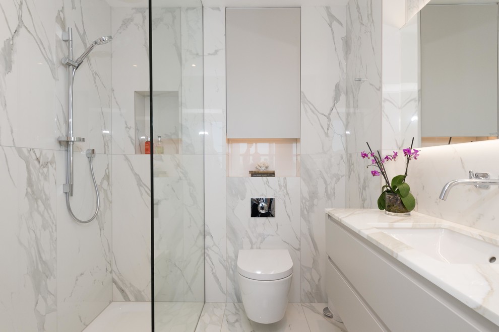 Inspiration for a medium sized contemporary shower room bathroom in London with flat-panel cabinets, white cabinets, a shower/bath combination, a wall mounted toilet, marble tiles, marble flooring, white floors, white tiles, a submerged sink, marble worktops and an open shower.