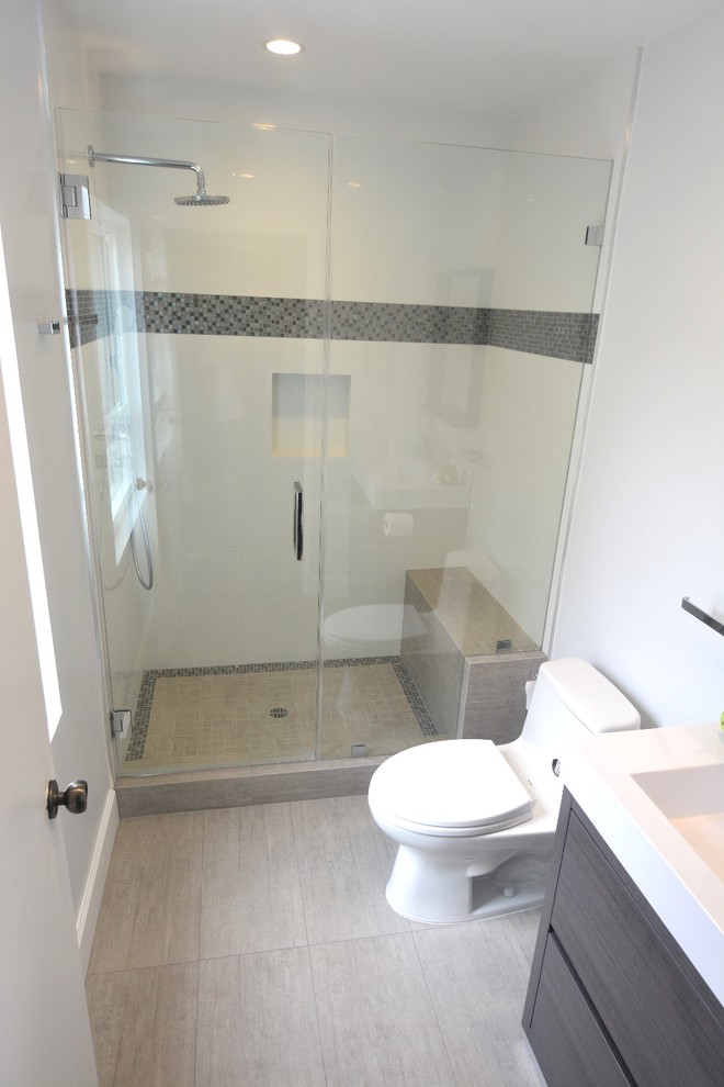 Modern inredning av ett litet badrum med dusch, med skåp i mörkt trä, en öppen dusch, en toalettstol med hel cisternkåpa, flerfärgad kakel, vita väggar, ljust trägolv, ett nedsänkt handfat och släta luckor