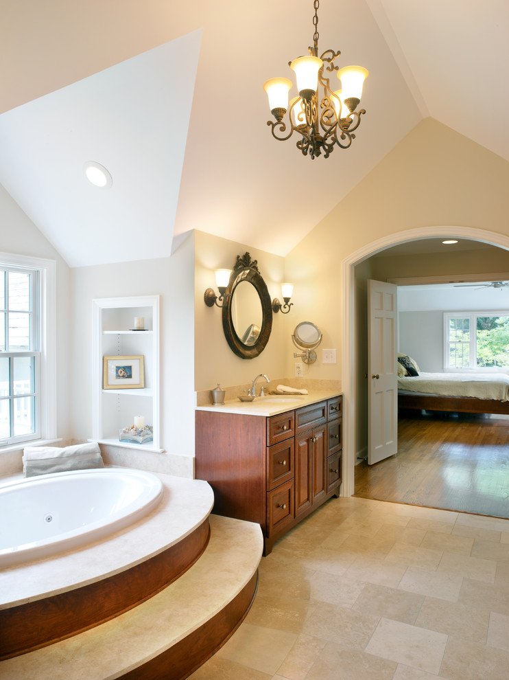 Idée de décoration pour une salle de bain principale tradition en bois brun avec un lavabo encastré, un placard avec porte à panneau encastré, un plan de toilette en calcaire, un bain bouillonnant, un carrelage beige, un mur beige et un sol en carrelage de porcelaine.