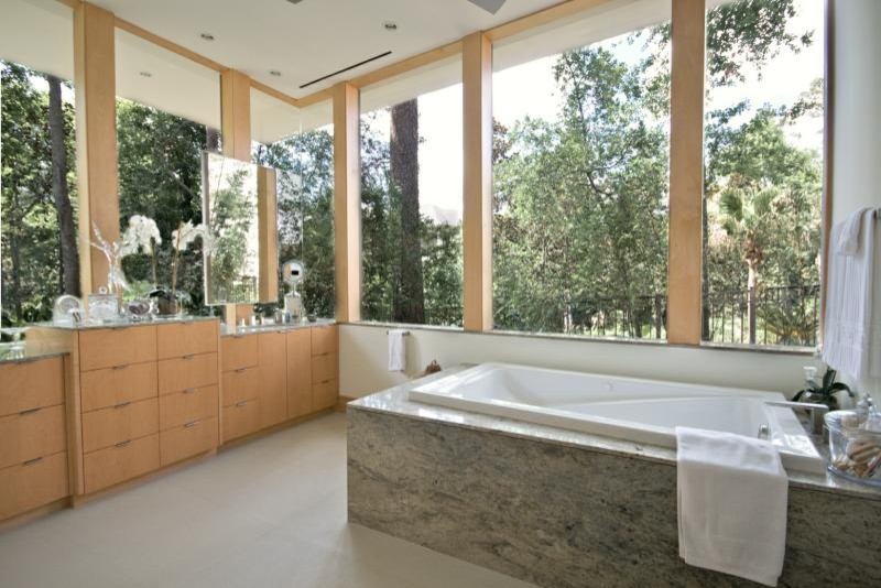 Imagen de cuarto de baño principal actual de tamaño medio con puertas de armario de madera clara, bañera encastrada, armarios con paneles lisos, paredes blancas, suelo de piedra caliza y encimera de granito
