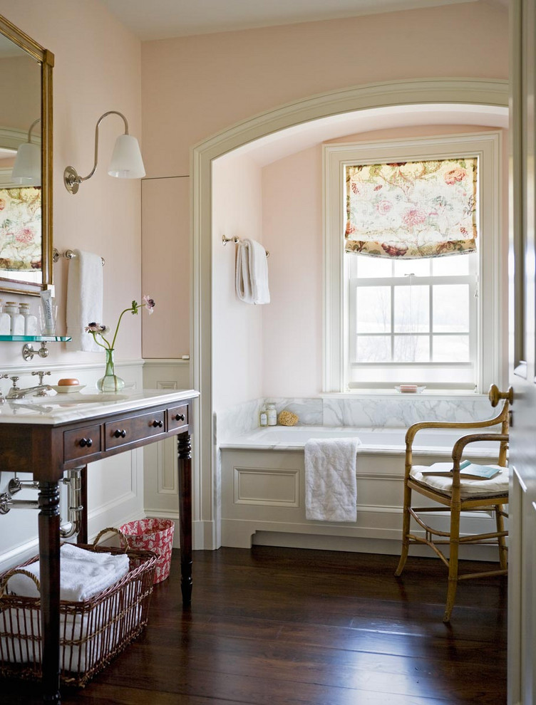 На фото: главная ванная комната в классическом стиле с темными деревянными фасадами, ванной в нише, розовыми стенами, темным паркетным полом, врезной раковиной, коричневым полом, белой столешницей, тумбой под одну раковину, напольной тумбой и панелями на стенах с