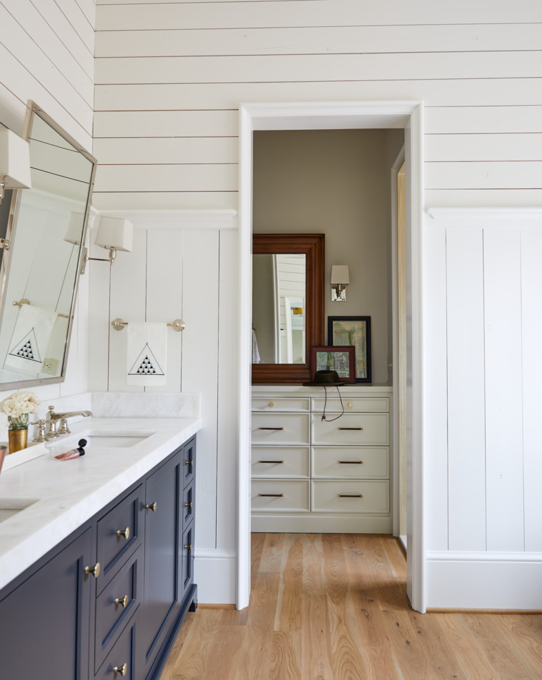 Modelo de cuarto de baño principal campestre con armarios tipo mueble, ducha doble, paredes blancas, suelo de madera clara y encimera de madera