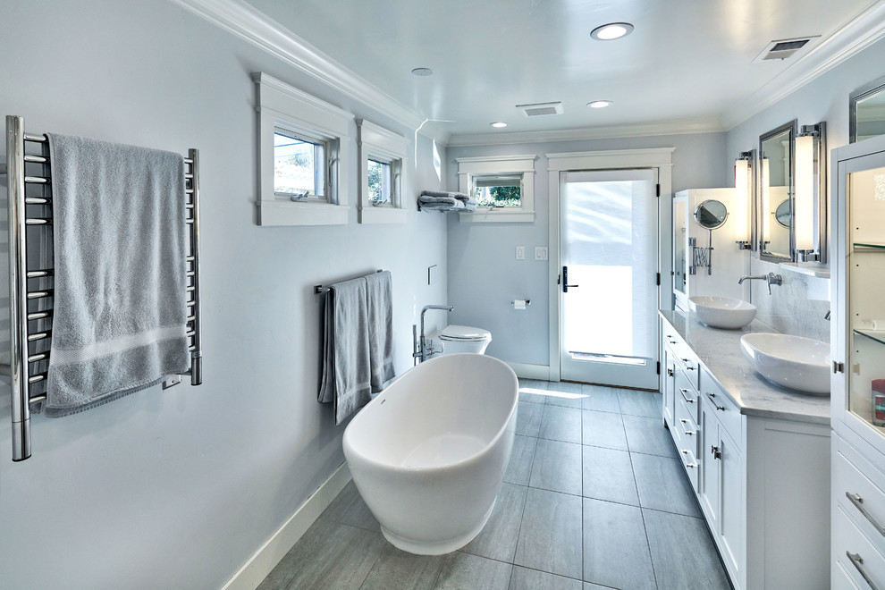 Klassisk inredning av ett stort en-suite badrum, med skåp i shakerstil, vita skåp, ett fristående badkar, en dubbeldusch, en vägghängd toalettstol, vit kakel, tunnelbanekakel, grå väggar, kalkstensgolv, ett fristående handfat och marmorbänkskiva