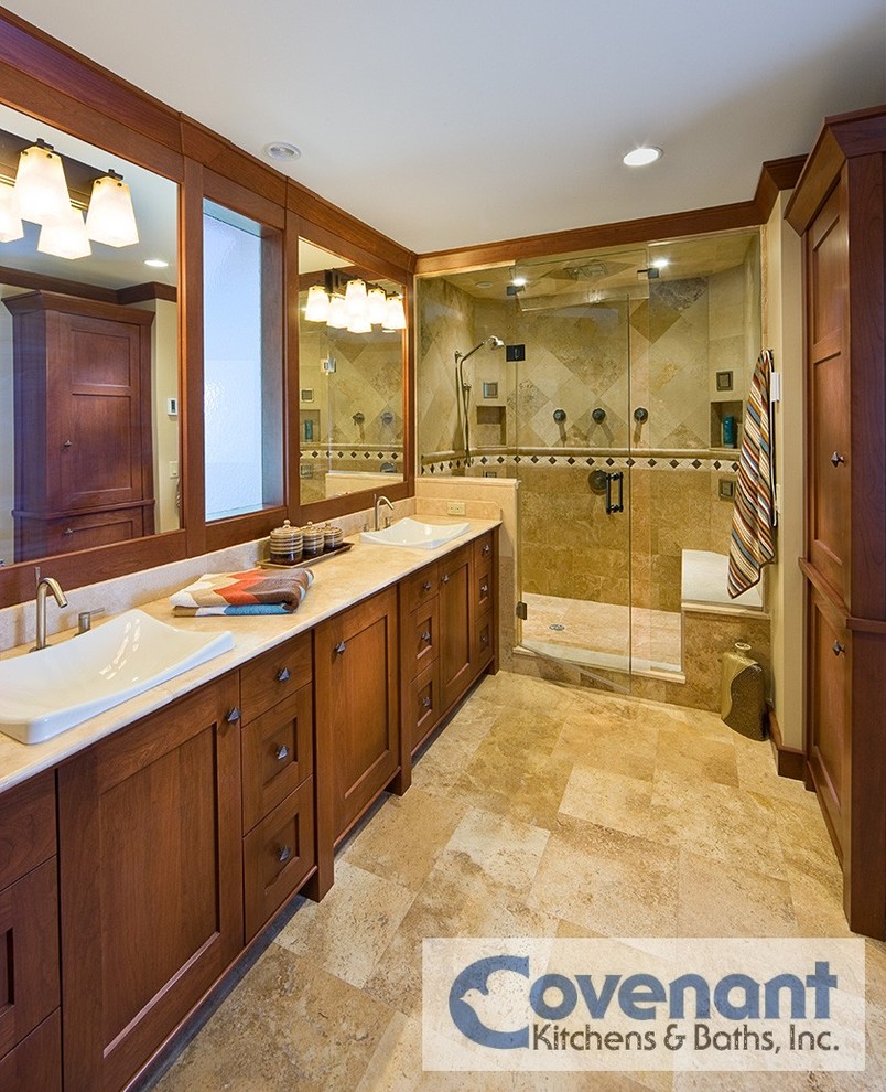 Inredning av ett amerikanskt badrum, med ett fristående handfat, skåp i mellenmörkt trä, en dusch i en alkov, beige kakel, stenkakel, travertin golv och skåp i shakerstil