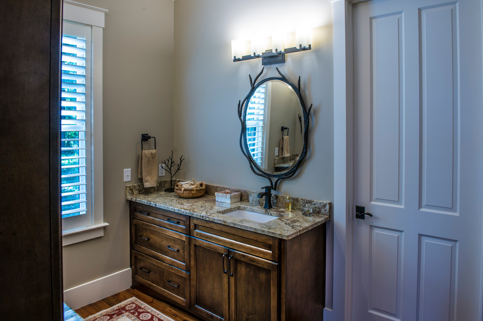 Cette image montre une salle de bain principale traditionnelle en bois foncé de taille moyenne avec un placard en trompe-l'oeil, un sol en bois brun, un plan de toilette en granite, un lavabo encastré et un mur gris.