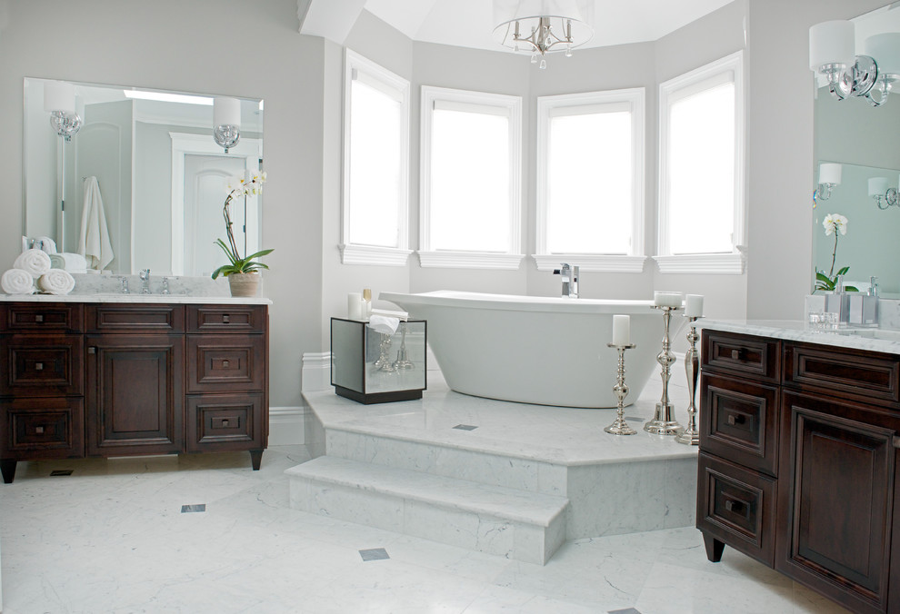 Design ideas for a large traditional ensuite bathroom in New York with a submerged sink, dark wood cabinets, marble worktops, a freestanding bath, a corner shower, a one-piece toilet, grey tiles, stone slabs, grey walls and marble flooring.