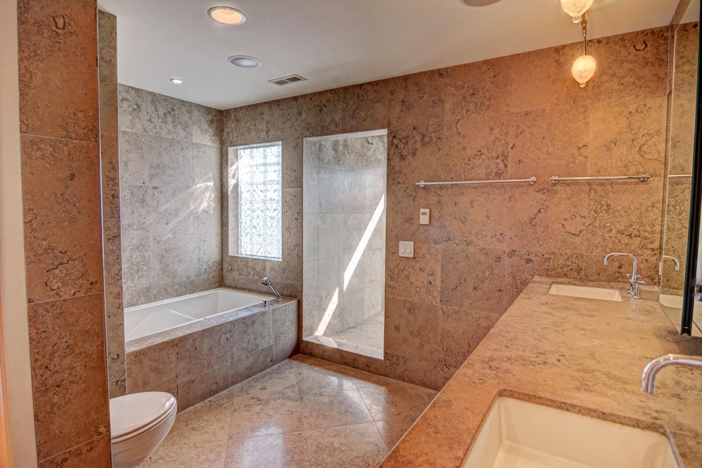 Idée de décoration pour une grande salle de bain principale design en bois clair avec un plan de toilette en granite, un carrelage beige, un carrelage de pierre, une baignoire posée, une douche ouverte, WC suspendus, un lavabo encastré, un mur beige, un sol en travertin et un placard à porte plane.
