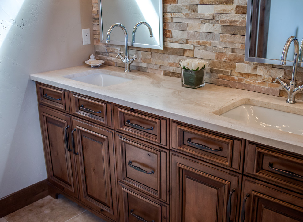 Example of a large classic master beige tile and stone slab porcelain tile and brown floor bathroom design in Denver with raised-panel cabinets, dark wood cabinets, a one-piece toilet, beige walls, an undermount sink and limestone countertops