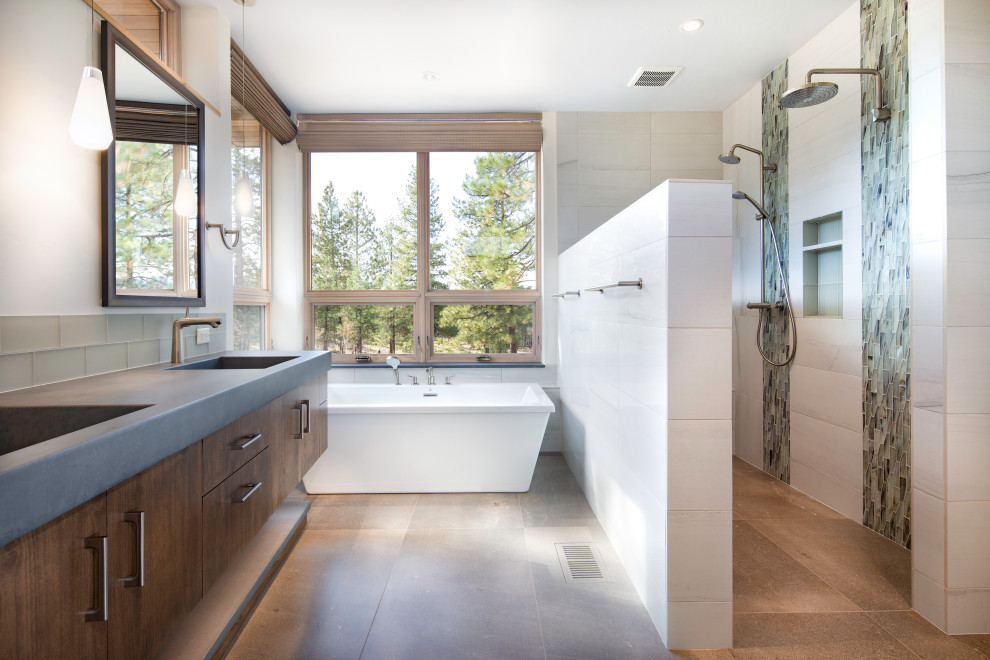 Пример оригинального дизайна: большая главная ванная комната в современном стиле с плоскими фасадами, темными деревянными фасадами, отдельно стоящей ванной, двойным душем, зеленой плиткой, стеклянной плиткой, белыми стенами, монолитной раковиной, столешницей из бетона, открытым душем и серой столешницей
