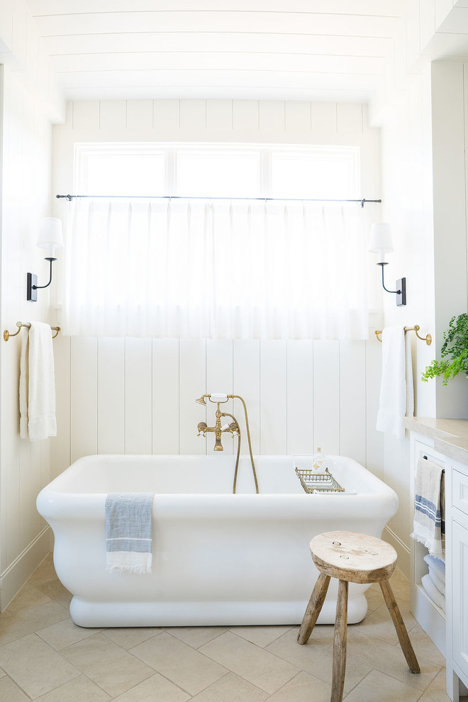 This is an example of a coastal bathroom in Orange County with a freestanding bath, white walls and beige floors.