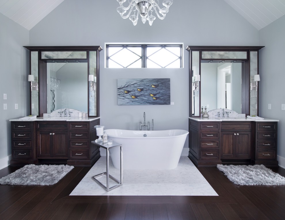 Klassisk inredning av ett mycket stort badrum, med ett undermonterad handfat, luckor med infälld panel, skåp i mörkt trä, marmorbänkskiva, ett fristående badkar, en toalettstol med separat cisternkåpa, vit kakel, stenhäll, grå väggar och bambugolv