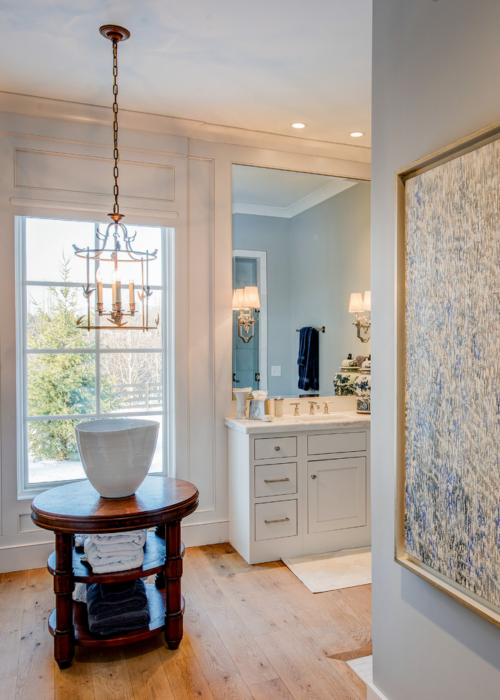 Ejemplo de cuarto de baño principal clásico renovado grande con armarios estilo shaker, puertas de armario blancas, paredes blancas, suelo de madera en tonos medios, lavabo bajoencimera y encimera de mármol