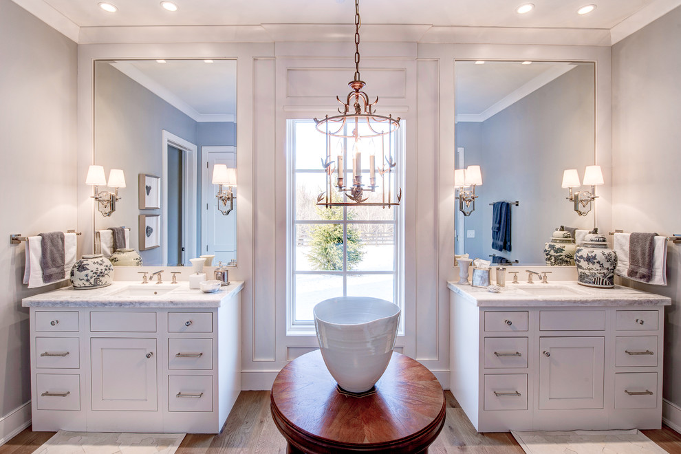 Ejemplo de cuarto de baño principal clásico renovado grande con armarios estilo shaker, puertas de armario blancas, paredes blancas, suelo de madera en tonos medios, lavabo bajoencimera y encimera de mármol