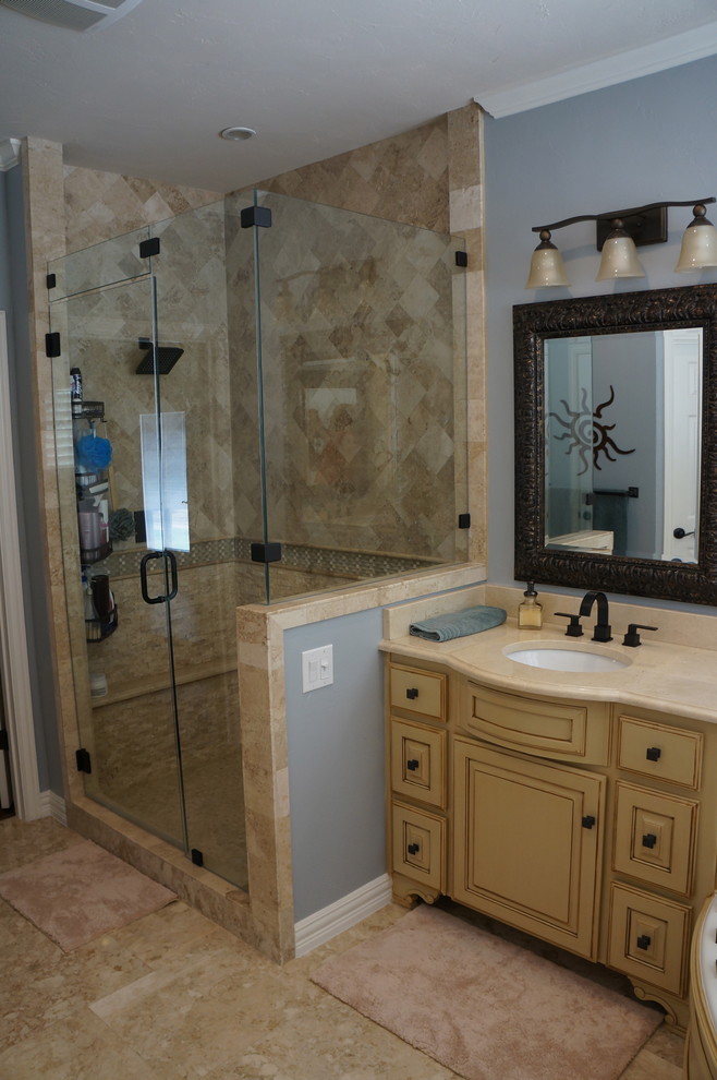 Photo of a medium sized traditional ensuite bathroom in Dallas with a submerged sink, raised-panel cabinets, distressed cabinets, marble worktops, a corner shower, a one-piece toilet, beige tiles, stone tiles, blue walls and travertine flooring.