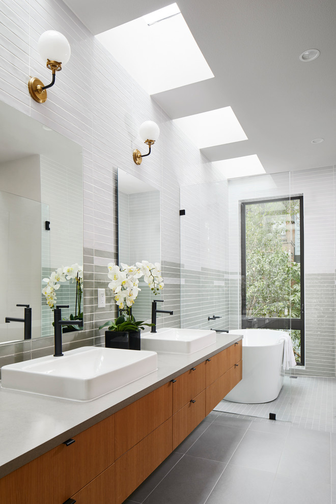 Idéer för ett modernt en-suite badrum, med släta luckor, skåp i mellenmörkt trä, ett fristående badkar, grå kakel, flerfärgad kakel, vit kakel, ett fristående handfat och grått golv
