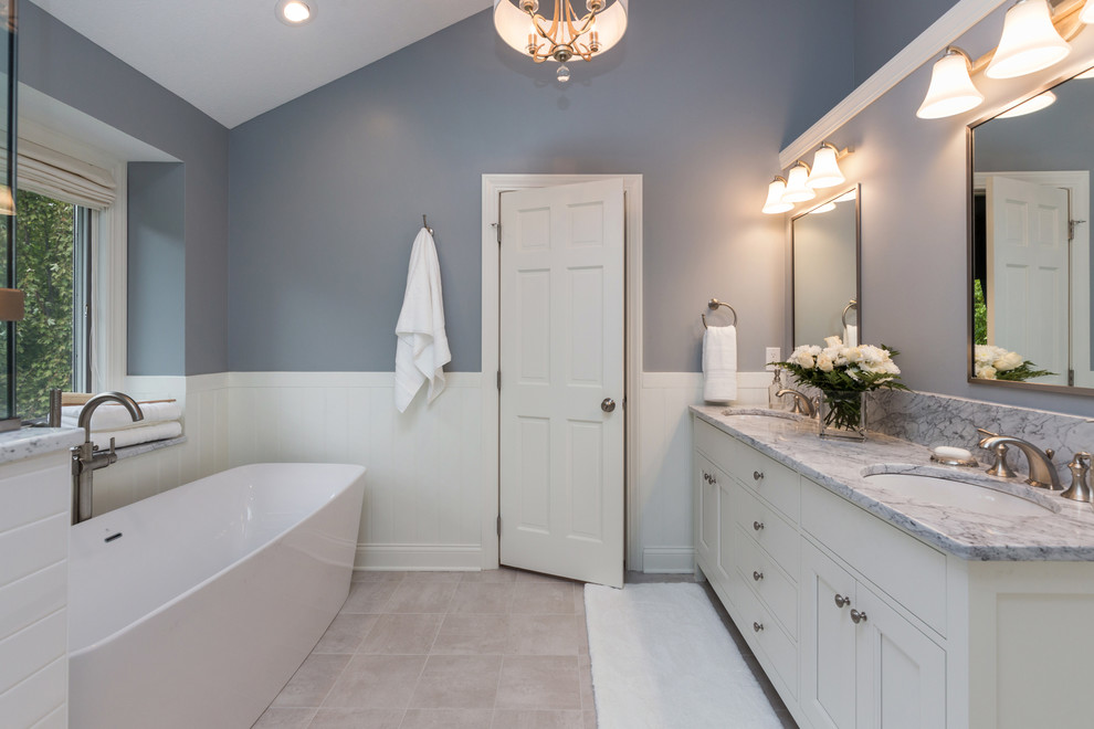 Foto på ett mellanstort vintage en-suite badrum, med ett undermonterad handfat, möbel-liknande, vita skåp, marmorbänkskiva, ett fristående badkar, en dubbeldusch, en toalettstol med separat cisternkåpa, grå väggar och klinkergolv i keramik