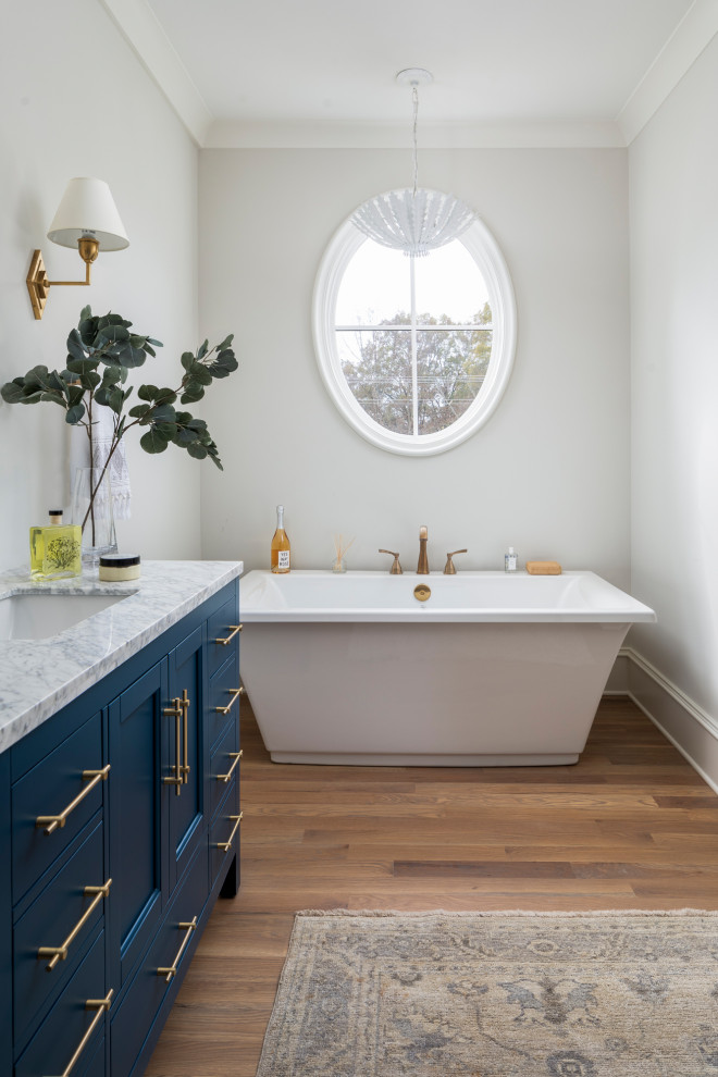 Immagine di una stanza da bagno padronale costiera di medie dimensioni con ante blu, vasca freestanding, pareti beige, pavimento in legno massello medio, un lavabo e mobile bagno freestanding
