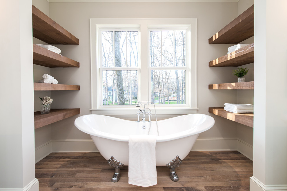 Amerikansk inredning av ett mellanstort en-suite badrum, med ett badkar med tassar, beige väggar, ljust trägolv och beiget golv