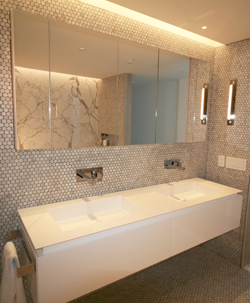 Inredning av ett modernt mycket stort en-suite badrum, med släta luckor, vita skåp, ett fristående badkar, en kantlös dusch, grå kakel, stenhäll, vita väggar, betonggolv, ett väggmonterat handfat och bänkskiva i akrylsten