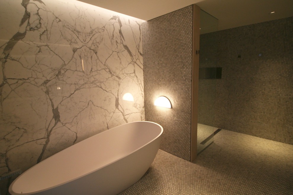 This is an example of an expansive contemporary ensuite bathroom in Other with flat-panel cabinets, white cabinets, a freestanding bath, a built-in shower, white tiles, stone slabs, white walls, concrete flooring, a wall-mounted sink and solid surface worktops.