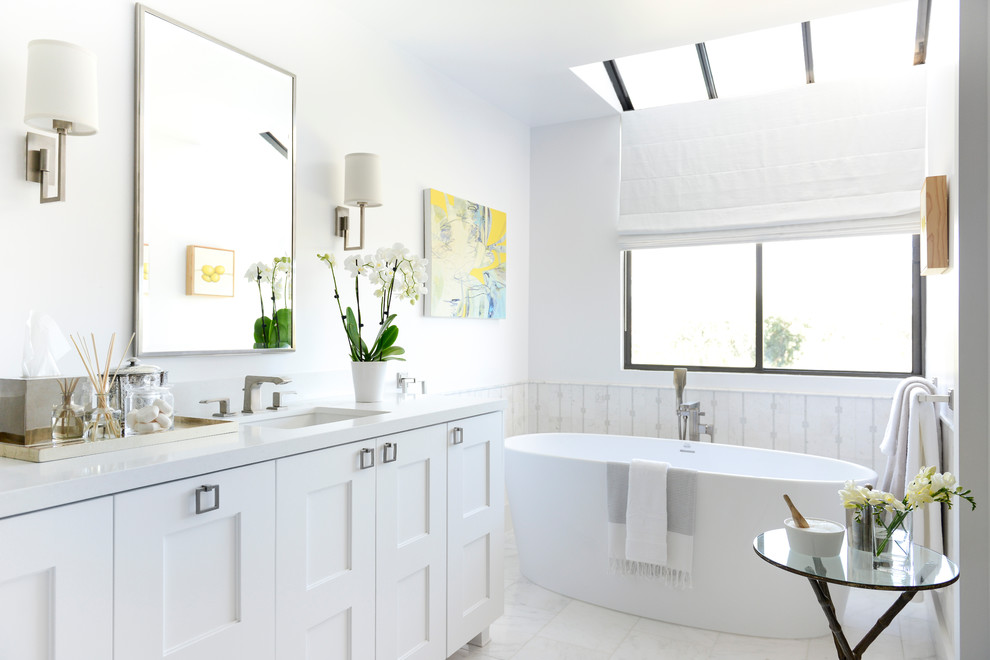 На фото: главная ванная комната среднего размера в стиле неоклассика (современная классика) с фасадами в стиле шейкер, белыми фасадами, отдельно стоящей ванной, белой плиткой, плиткой мозаикой, белыми стенами, мраморным полом, врезной раковиной и столешницей из искусственного камня с